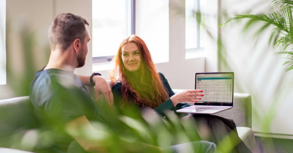Prosjektstyring i Business Online: To kollegaer diskuterer prosjektstatus foran en laptop